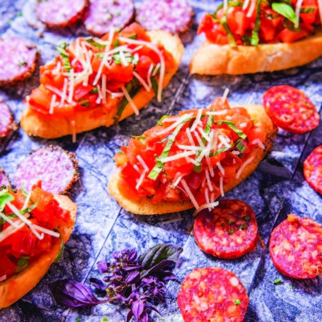 slices of baguette bread topped with chopped tomato, herbs, and cheese. laying on top of sliced salami