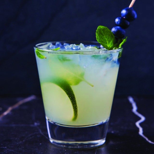 Mixed drink with lime, mint and blueberry garnish