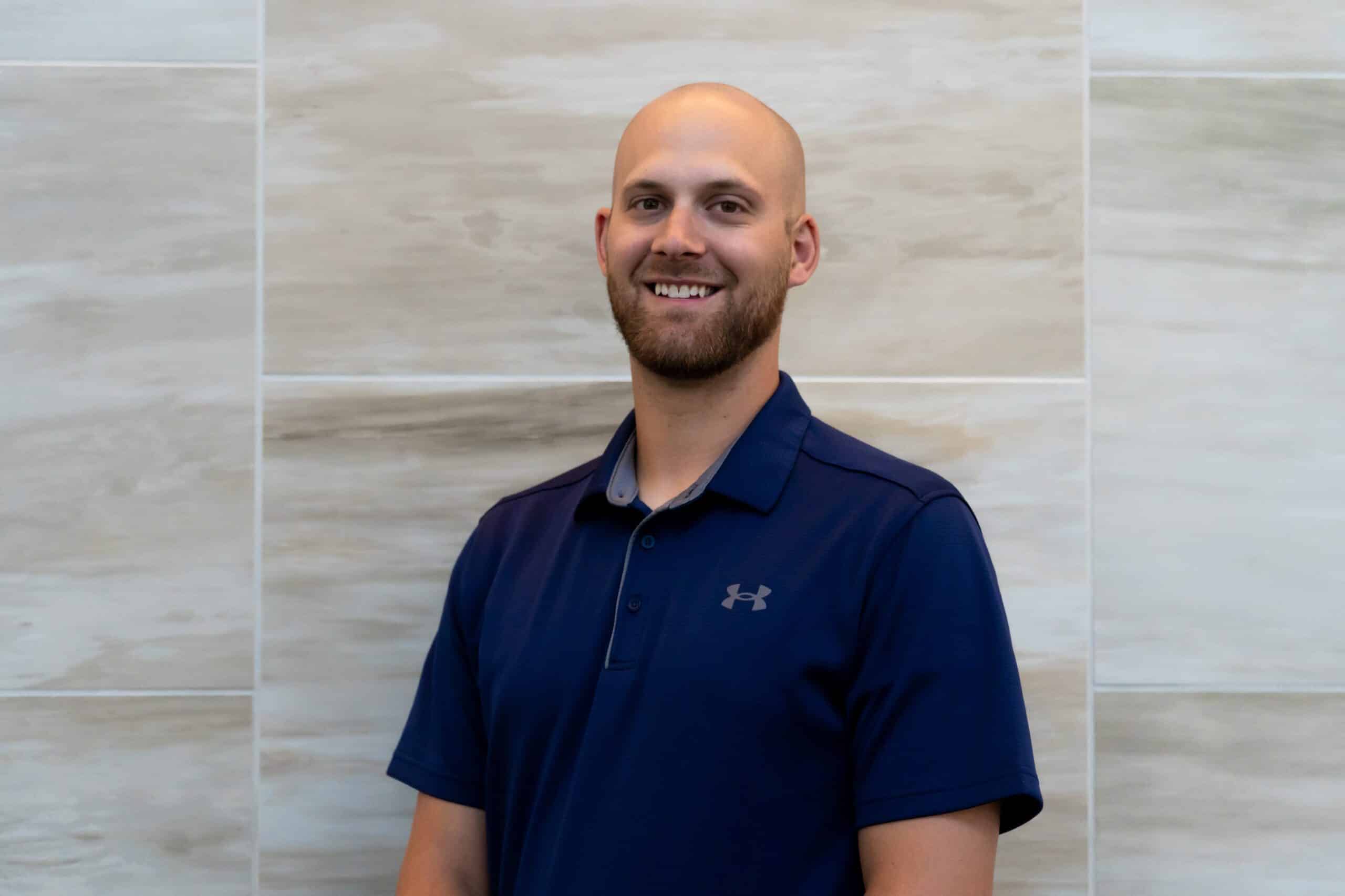 bald man with a brown beard wearing a blue polo shirt.