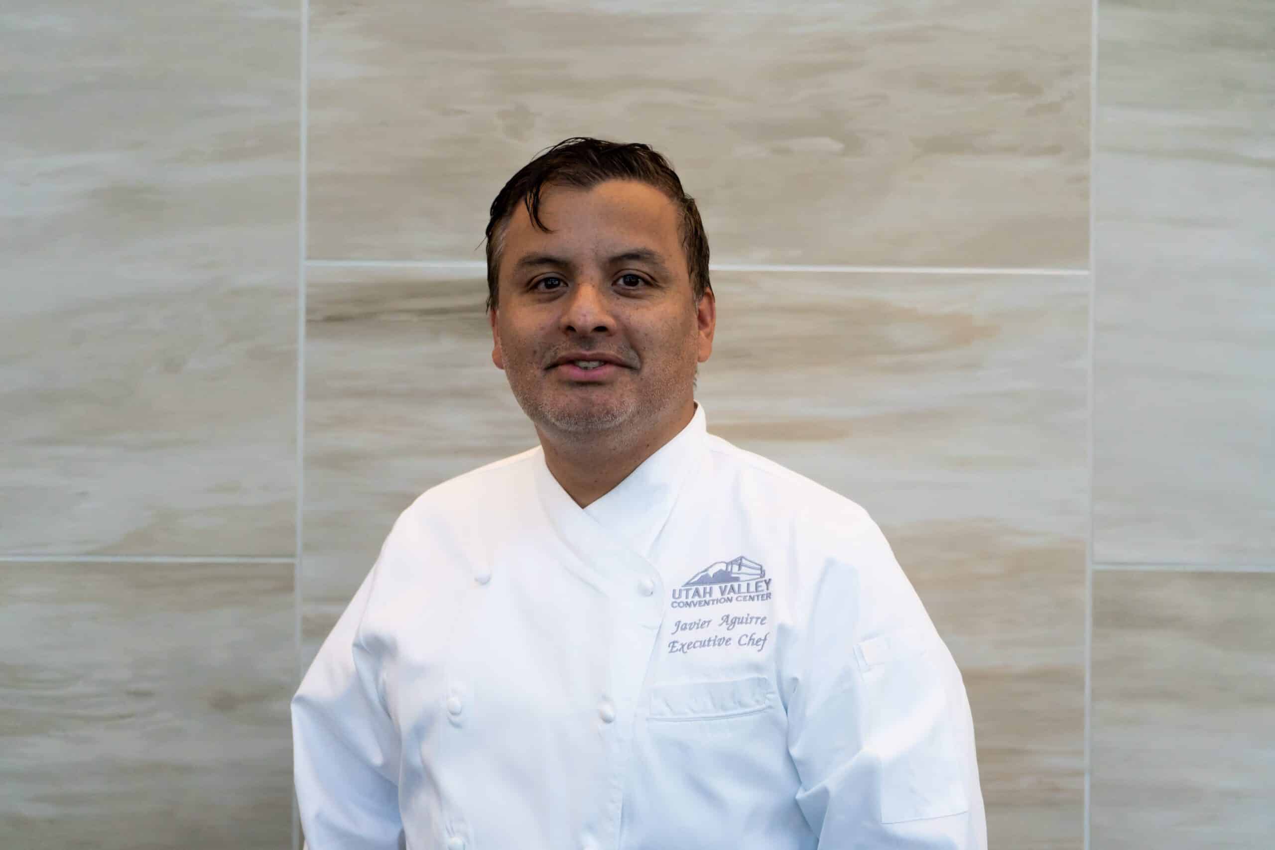 man with dark brown hair, light facial hair, wearing a white chef coat.