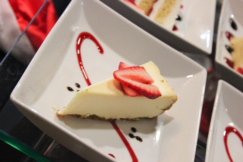 piece of cheesecake with straberries on top, garnished with pink and chocolate sauces
