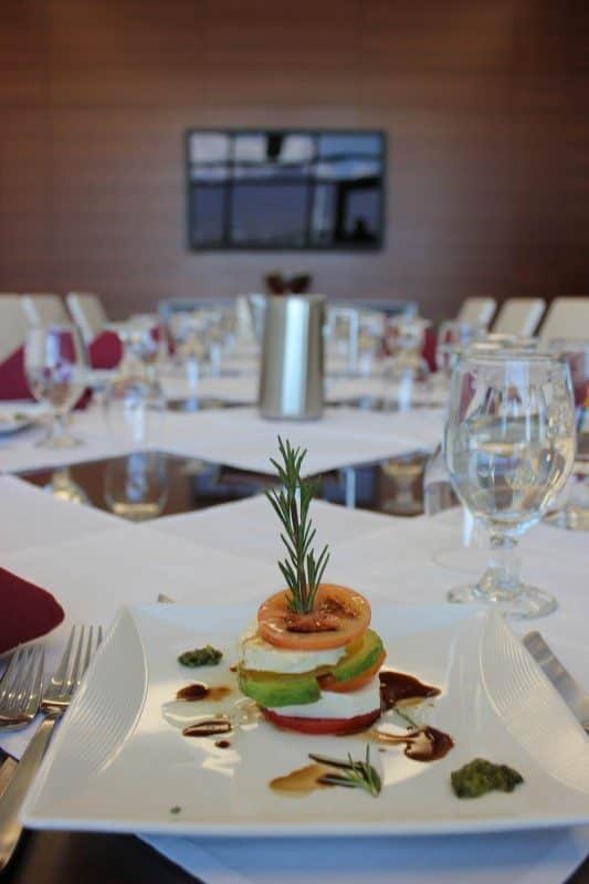plate with a salad on it--layers of tomato and cheese with various condiments around it additional place settings in the background.