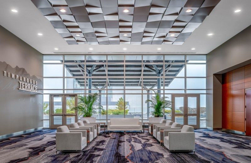 Modern lobby with geometric ceiling, large windows, and white armchairs
