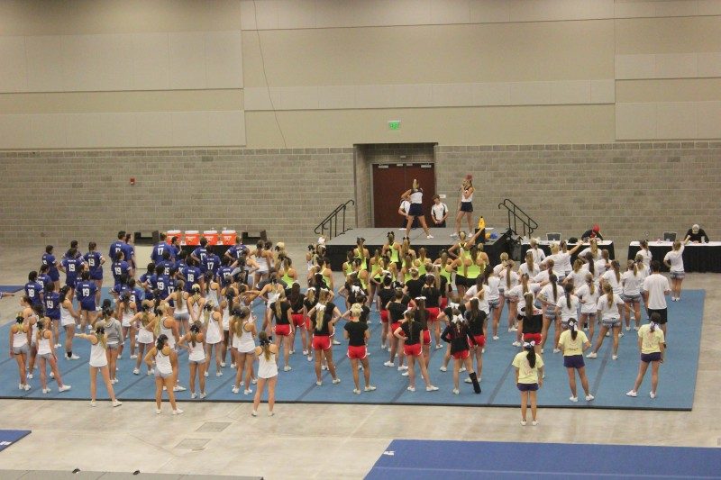 Many cheerleaders practicing on blue mats inside a large room