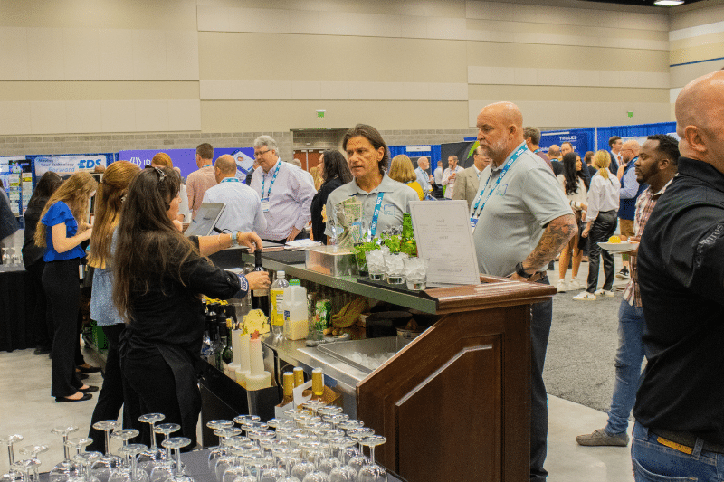 People at a convention center with a bar setup and drinks on a counter