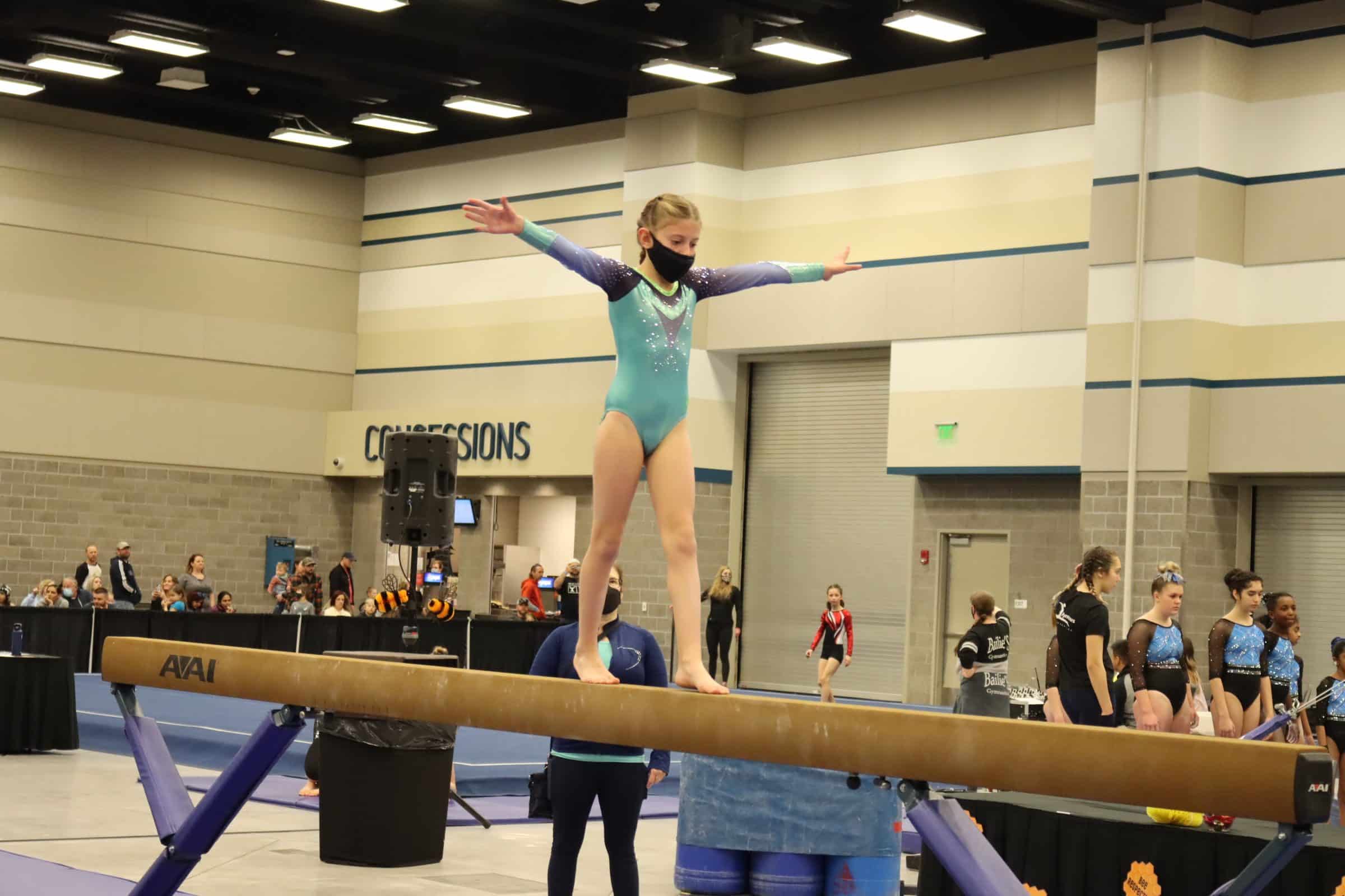 young girl wearing facemask competing on the balance beam