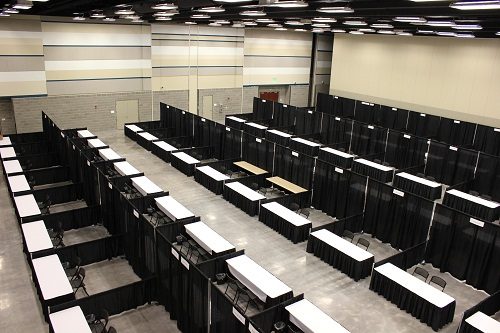 Empty convention hall with rows of black partitioned booths and tables