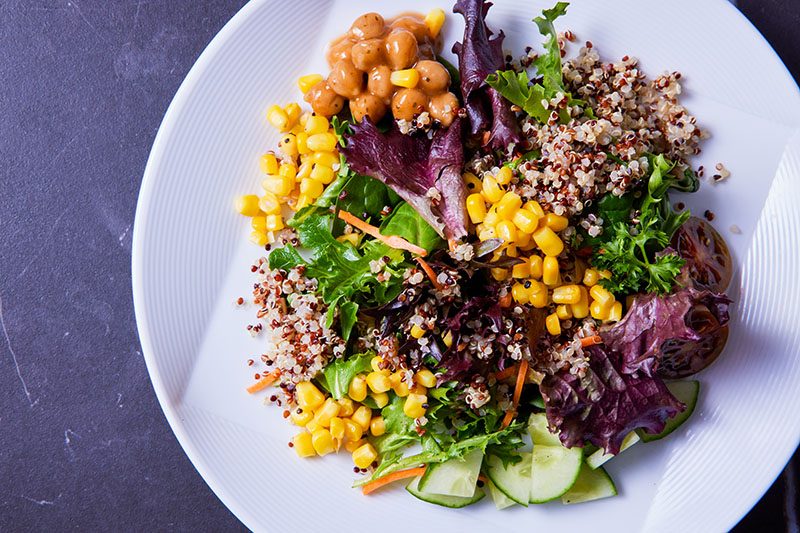 bright colored salad with chickpea, corn, various lettuces, cucumber, and quinoa