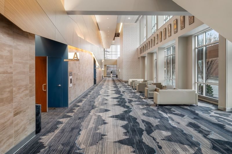 Modern hallway with patterned carpet, seating areas, and large windows
