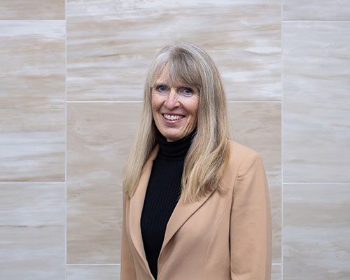 Person with blonde hair in a beige blazer and black top
