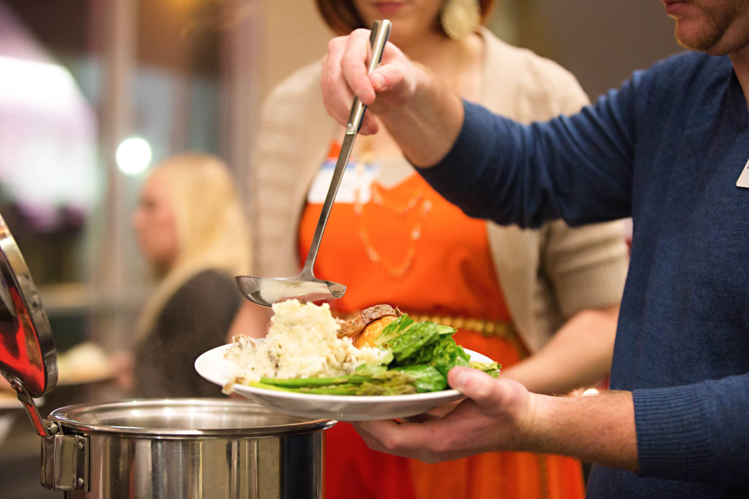 Person serving food onto a plate at a buffet