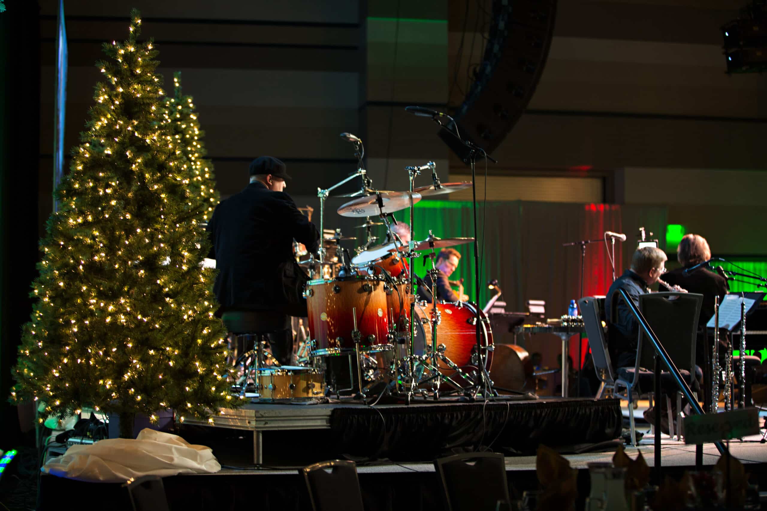 A drummer on stage near a lit Christmas tree with band members